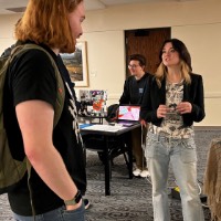 Man and woman talking to each other in front of screen that says Soph's Studio